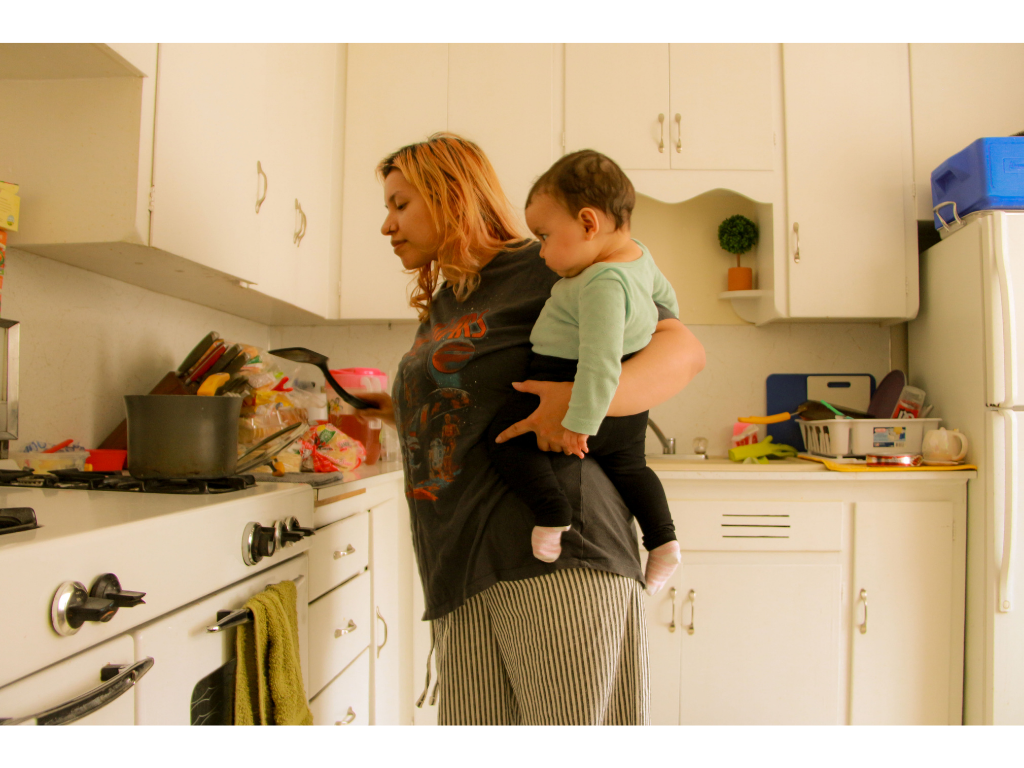 Woman cooking in kitchen with child on her hip